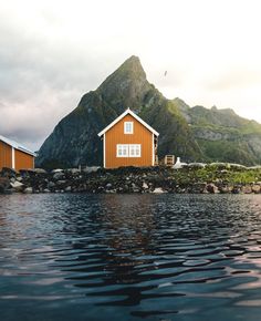 two red houses sitting on top of a lake next to a large mountain covered in clouds