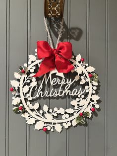 a merry christmas wreath hanging on the wall with a red bow and ribbon attached to it