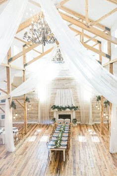 an indoor wedding venue with wooden floors and white drapes on the ceiling, decorated with greenery