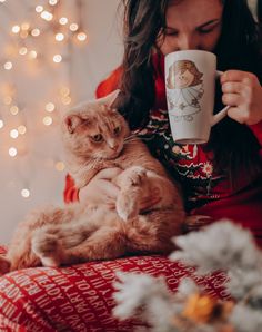 a woman is holding a cat and drinking from a coffee cup