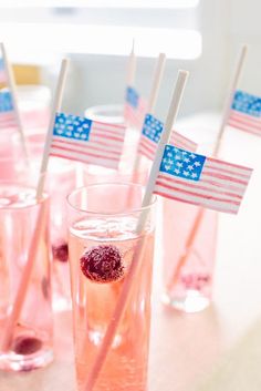 three glasses filled with pink liquid and american flags on top of each glass, sitting on a table