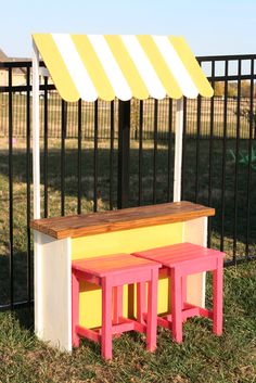 a bench and table in front of a black fence with yellow awning over it