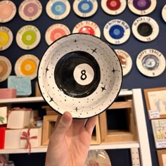 a person holding up a black and white bowl with eight ball on it in front of a wall full of colorful plates