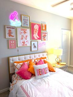 a white bed topped with lots of pillows under pictures on the wall next to a lamp