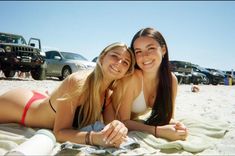 two young women laying on the beach in front of their cars and smiling at the camera