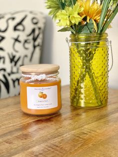 a jar of honey sitting on top of a wooden table next to a vase with flowers