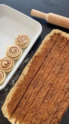 some cinnamon rolls are sitting on a table next to a baking pan and rolling pinwheels