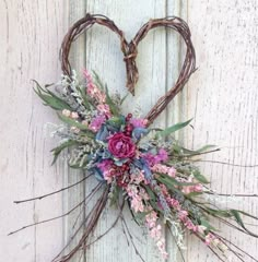 a heart shaped wreath with pink flowers hanging on a white wooden door, decorated with branches and twigs