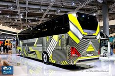 a yellow and black bus is on display in a building with people walking around it