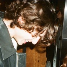 a young man looking down at his cell phone while standing next to a woman in a black jacket