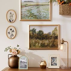 three framed pictures hang on the wall above a wooden table with vases and flowers