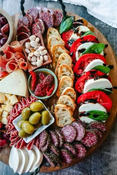 an assortment of meats and cheeses on a wooden platter with olives