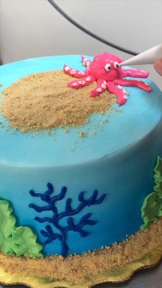 a blue cake with an octopus on top and sand in the ocean around it is being frosted