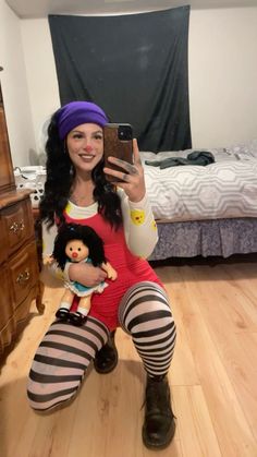 a woman sitting on the floor taking a selfie with her cell phone and doll