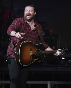 a man holding a guitar in his right hand and singing into the microphone on stage