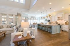 a large open concept kitchen and living room with hardwood floors, white cabinets, an island in the center