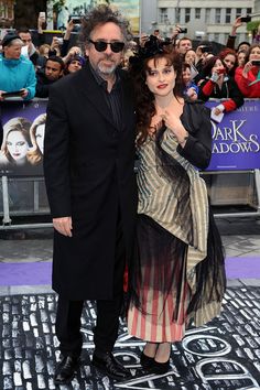 a man and woman standing next to each other on a purple carpet with people in the background