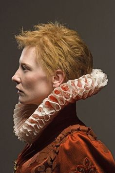 a woman with short red hair wearing an orange dress and white ruffled neck scarf