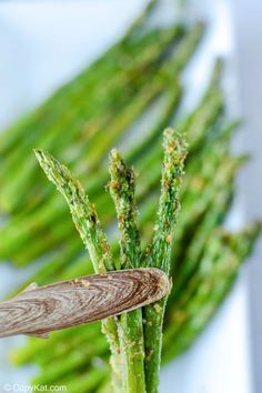 asparagus spears are being held by a wooden spoon