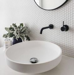 a white bathroom sink sitting under a round mirror next to a black faucet