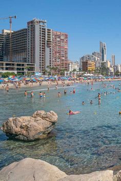 many people are swimming in the ocean near some buildings