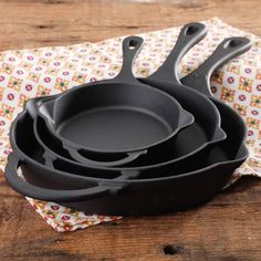 four cast iron skillets sitting on top of a wooden table next to a napkin