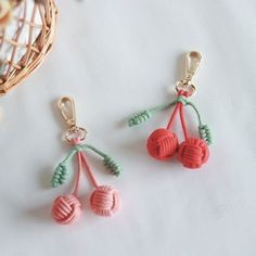 two crocheted cherries hanging from hooks on a white tablecloth next to a basket