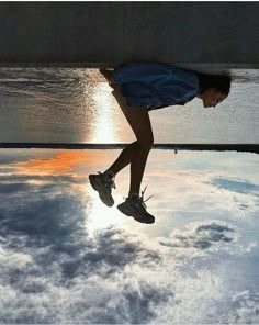 a person jumping in the air with their shoes on and clouds reflected in the water