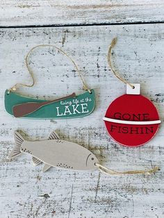 three wooden ornaments hanging from strings on a white wood background with words gone fishin, fishing life is the lake and gone fishin