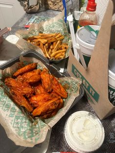 chicken wings and french fries in takeout containers on a table with condiments