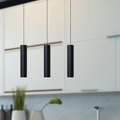 three black lights hanging from the ceiling above a kitchen sink and countertop with white cabinets