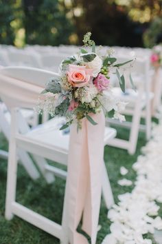 an outdoor wedding ceremony with white chairs and pink flowers on the back of each chair