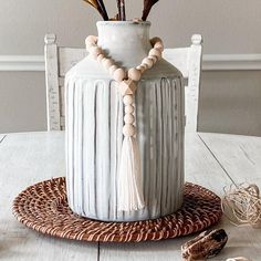 a white vase sitting on top of a wooden table next to a string of beads