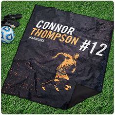 there is a black and yellow towel on the grass with other items around it that include a soccer ball