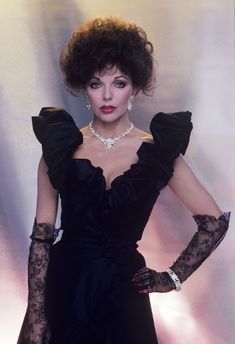 a woman in black dress and gloves posing for the camera with her hands on her hips