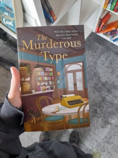 a person holding up a book in front of a table and bookshelf filled with children's books