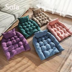 four different colors of dog beds sitting on the floor in front of a white couch