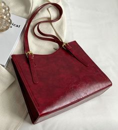 a red purse sitting on top of a bed next to a white sheet and glass vase