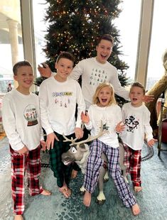 a group of kids standing next to each other in front of a christmas tree with reindeer pajamas on