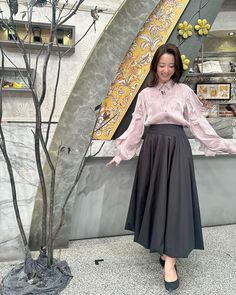 a woman standing next to a tree in front of a wall with art work on it