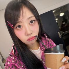 a woman holding a coffee cup with a straw in her mouth and wearing pink lipstick