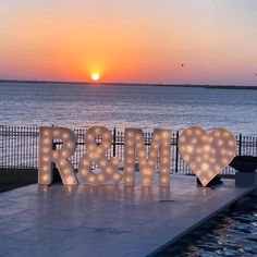 the letters r and m are lit up in front of an ocean at sunset or dawn