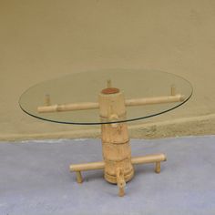 a round glass table with wooden legs on concrete flooring next to a beige wall