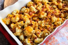 a casserole dish with bacon and cheese in it sitting on a table next to a wooden spoon