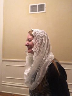 a woman with a veil on her head is standing in front of a wall and smiling