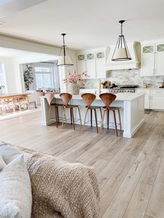 a kitchen with white cabinets and wooden flooring next to a dining room table filled with chairs