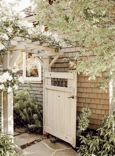 an old wooden door is open in front of a house with white flowers and greenery