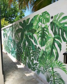 a white wall with green leaves painted on it and a brick walkway next to it