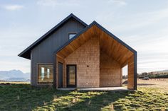 a small wooden house sitting on top of a lush green field with mountains in the background