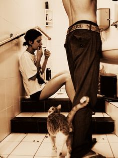 a man standing next to a woman in a bathroom with a cat on the floor